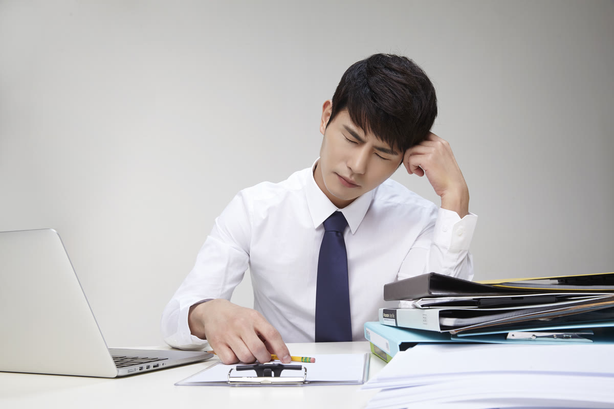 서류철이 쌓인 책상에 앉아 반려된 제출 서류를 앞에 두고 난감해하는 담당자의 모습