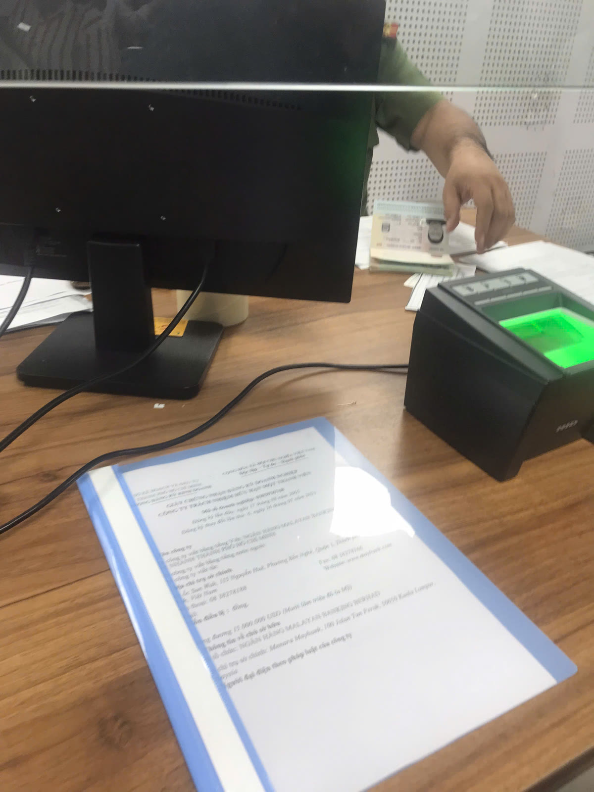 현지 관공서 창구 책상 위에 투명 파일에 끼운 베트남어 법인 서류와 지문 인식 장비가 놓여 있는 모습